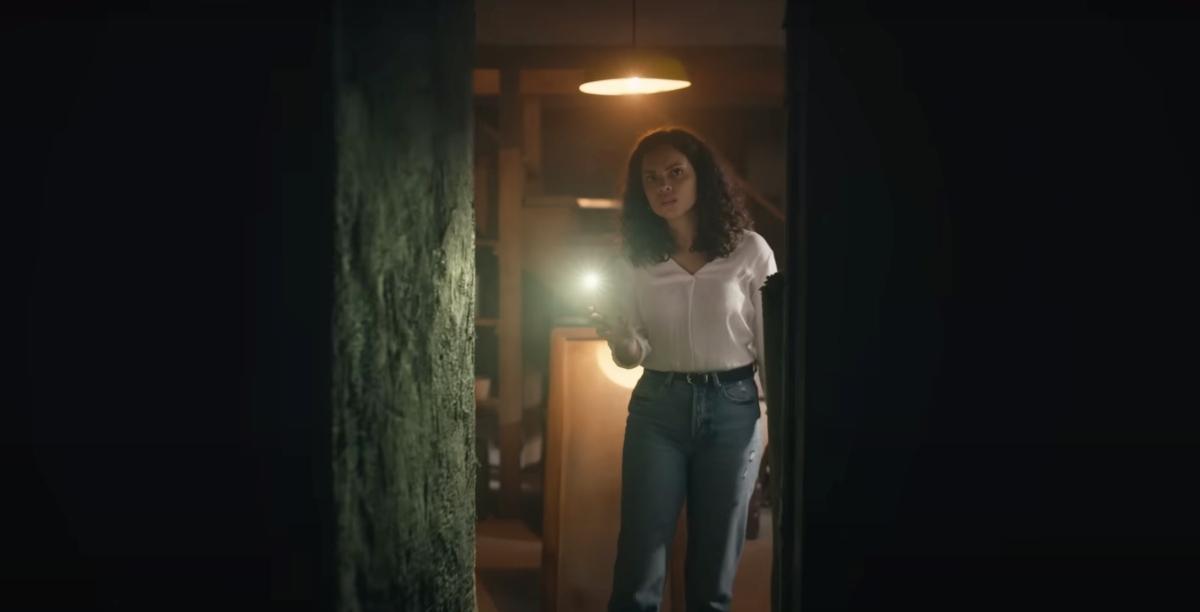 A still from the movie Barbarian showing star Georgina Campbell looking through a creepy, open doorway with a flashlight.